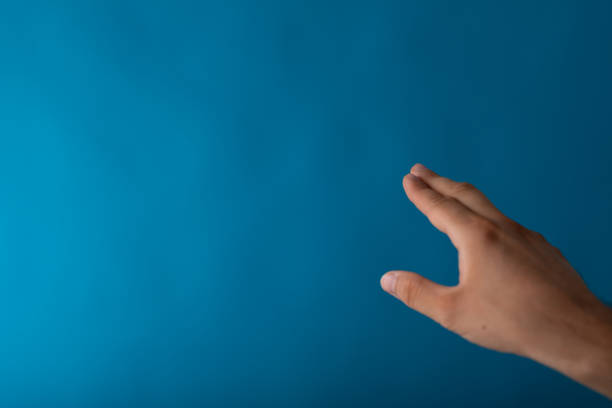 Closeup of a male shows an outstretched hand isolated on a blue background A closeup of a male shows an outstretched hand isolated on a blue background male is standing and shows outstretched hand with open palm stock pictures, royalty-free photos & images