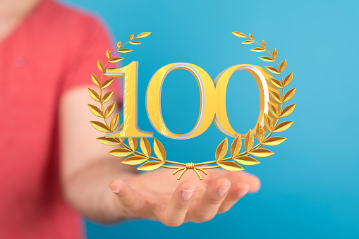 A 3d golden rendering of 100 with laurel wreath hovering over man's palms - anniversary and success concept