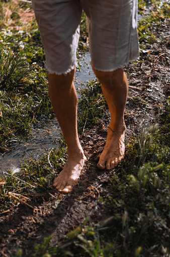A vertical shot of a person walking on the muddy ground with bare feet