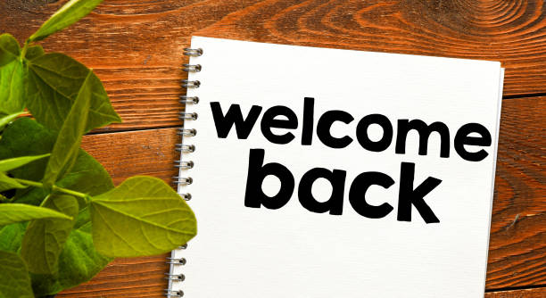 istock WELCOME BACK words written in a notebook on a wooden table. View from above. 1464707666