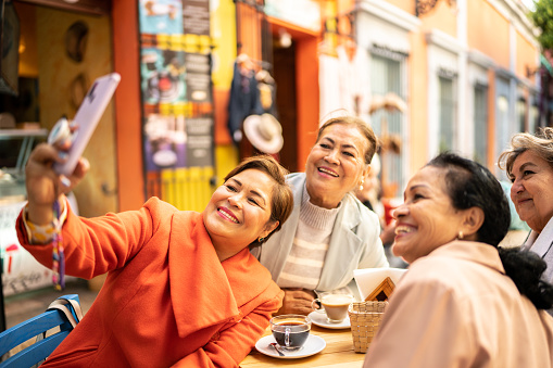 Senior friends taking a selfie or filming using mobile phone at coffee shop outdoors