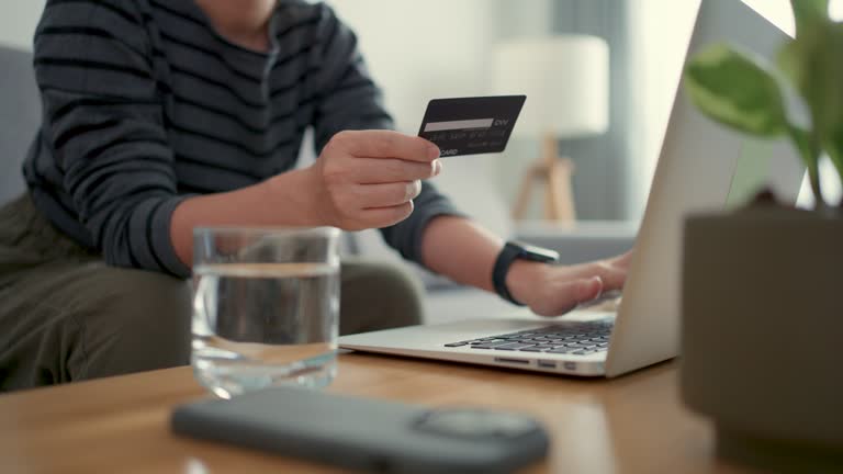 Female hands holding credit card using laptop paying for purchase on website shopping online in living room at home.