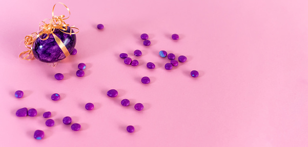 A close-up shot of a violet easter egg and candies on a pink background.