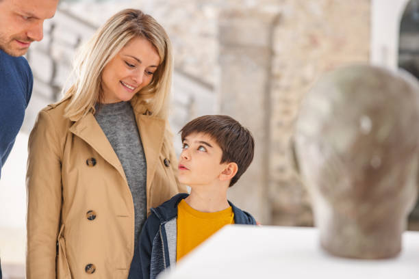un jeune fils de race blanche pose une question à ses parents alors qu’ils visitent un musée - child serious museum indoors photos et images de collection