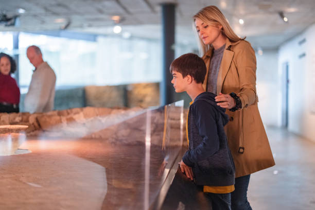 A Caucasian Mother Visiting A Museum With A Caucasian Young Son On A Weekend A caucasian mother taking her son to a history exhibition in a museum. The mother and her young son are looking through glass in order to see the artefacts displayed. The mother and son are serious and focused. The mother has her hand on the boy's shoulder. The boy looks interested. historical museum stock pictures, royalty-free photos & images