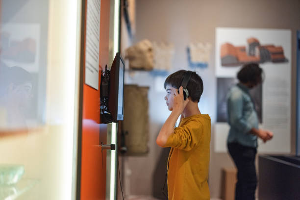 giovane ragazzo caucasico che mette le cuffie per ascoltare un'audioguida in un museo - one kid only audio foto e immagini stock