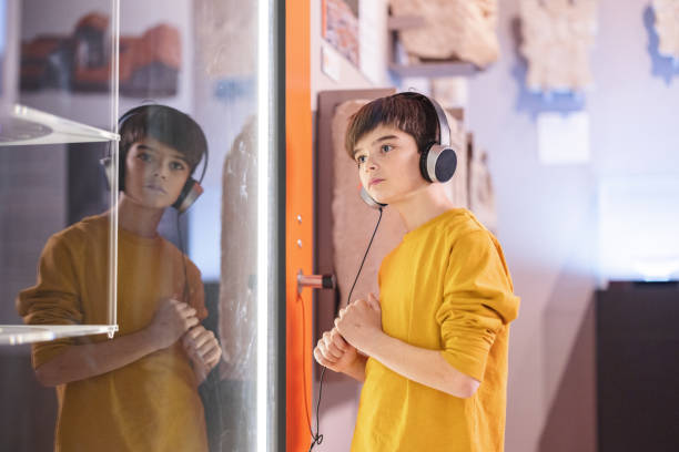 un jeune garçon de race blanche écoute un audioguide sur ses écouteurs tout en se promenant dans le musée - child serious museum indoors photos et images de collection