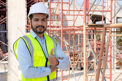 Portrait of young man is engineer wearing helmet smile with satisfied at construction site, architect or contractor standing and thumbs up with confidence, one person, worker or labor with handsome.