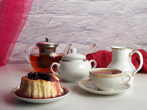 Сheesecake with cherry jam, black tea in a teapot, a cup with a drink, on a light background. Delicious and healthy breakfast.