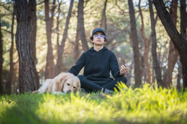 kleiner junge und sein hund verbringen zeit im wald und meditieren - zen like nature breathing exercise sitting stock-fotos und bilder