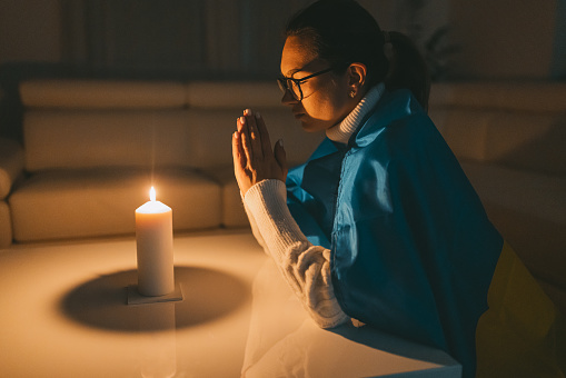 A woman with eyeglasses prays by candlelight for the war to end.