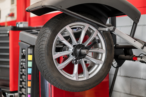 Wheel hanging on wheel balancer during car service inside of modern car dealer shop