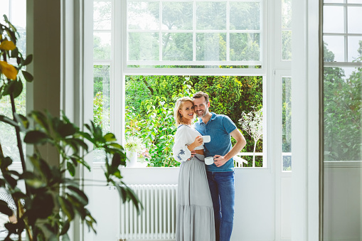 Portrait of happy couple with coffee cups standing near window at home