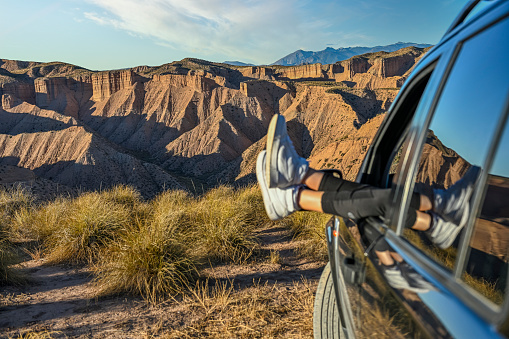 Young girl touching her feet through the car window, in the middle of a desert landscape