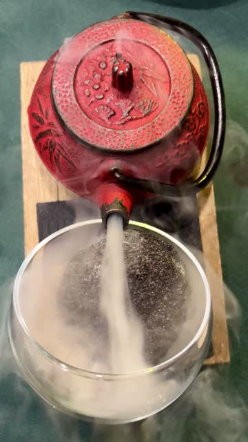 A classic teapot with smoke on a wooden table. classic red teapot with smoke over bowl on wooden table.