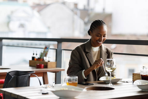 Black woman in restaurant A beautiful African-American woman is sitting on the restaurant's balcony, enjoying Italian pasta and a glass of white wine. georgijevic stock pictures, royalty-free photos & images