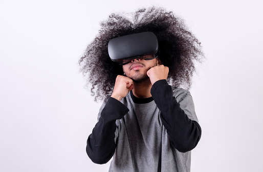 Playing a fighting game with virtual reality glasses. Young man with afro hair on white background