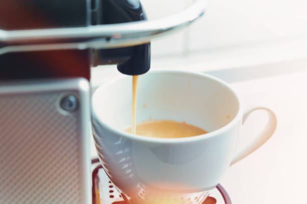 istock Fresh hot coffee runs out of a modern capsule machine into a white porcelain cup, colored light reflexes, bright background with copy space, selected soft focus 1464723097