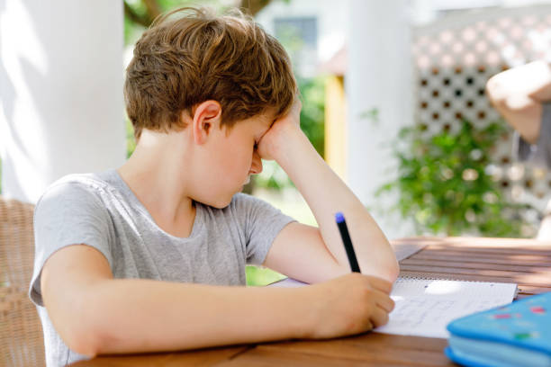 istock Hard-working sad school kid boy making homework during quarantine time from corona pandemic disease. Upset tired child on home schooling in coronavirus covid time, schools closed. 1464724485