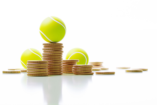 Tennis ball is sitting on coin stacks. Horizontal composition with copy space. Gambling and sports betting concept.