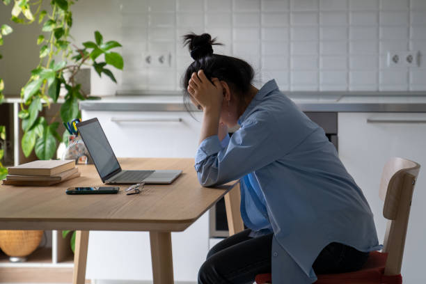 istock Overworked Asian girl sits at laptop holding head in hands thinks about problem professional burnout 1464724643