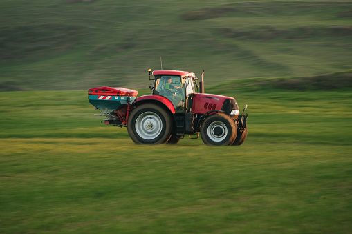 A modern tractor with a fertilizer machine in motion on an agricultural field