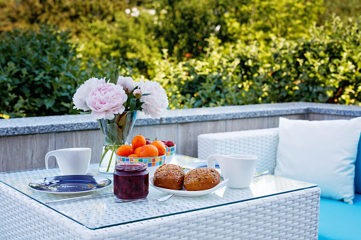 Breakfast table with bread, fresh fruits and strawberries and coffee served on balkony terrace or hotel on summer morning for romantic couple lunch
