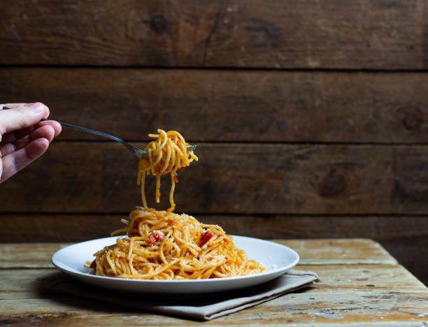 istock Pasta in tomato sauce on a fork over a plate. The hand holds the fork. Under the white plate is a brown napkin. 1464727374