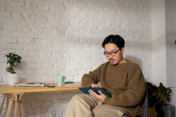 istock Chinese good-looking man with eyeglasses working on his tablet at his home office 1464727635