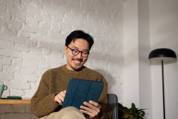 Happy modern Asian entrepreneur working on his tablet at home