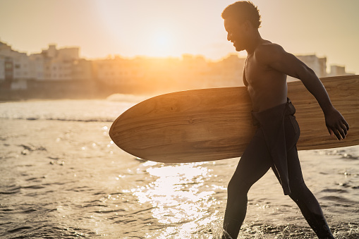 Male afro surfer having fun surfing during sunset time - African man enjoying surf day - Extreme sport lifestyle people concept