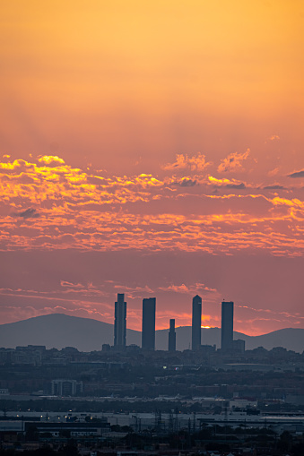 Orange sunset behind the Skyline and towers of the city of Madrid with buildings in silhouette.