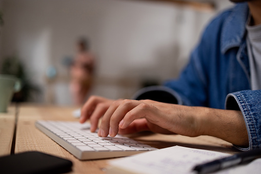 Hands of unrecognisable man typing on keyboard at wooden desk at home