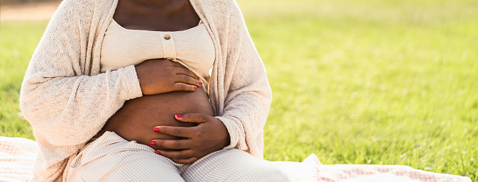 Close up pregnant belly of young African woman sitting in park - Maternity lifestyle concept