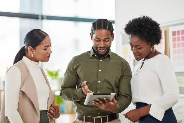 istock Team, black man and leader with tablet, fintech and conversation for planning, website launch and business success. Teamwork, African American male leader and women in modern office and search online 1464735792