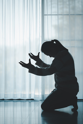 silhouette of woman kneeling and praying in modern church at sunset time. Female catholic prayer worship to God wish a better life in home at dawn with believe faith. concept of worshipers kneeling.