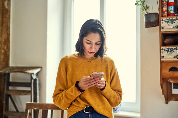 Serious woman text messaging on smart phone at home