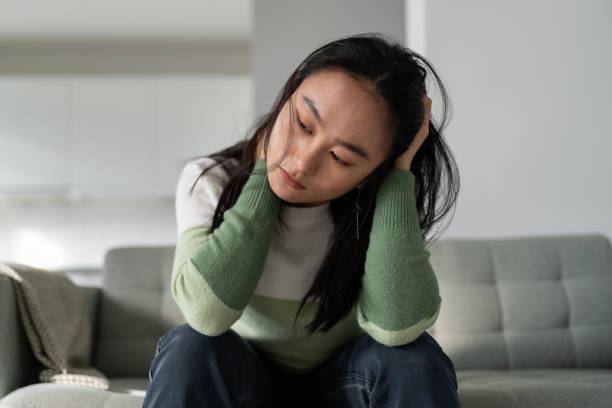 Unhappy depressed young Asian woman feeling sad and lonely after breakup or divorce Mental health, depression and anxiety. Unhappy Asian woman sits on sofa at home feeling sad, frustrated and lonely, dealing with breakup or divorce. Depressed Korean girl suffering from winter blues seasonal affective disorder stock pictures, royalty-free photos & images