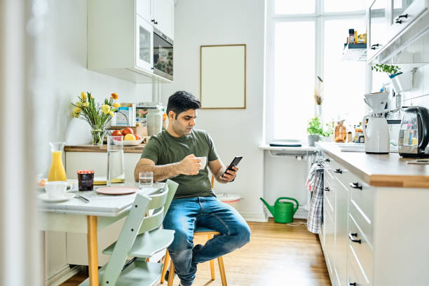 istock Mid adult man drinking coffee and using mobile phone in kitchen 1464739634