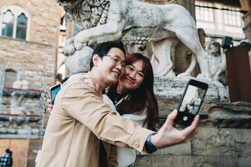 An asian couple is taking a selfie  in Florence, Italy. They are embracing together.