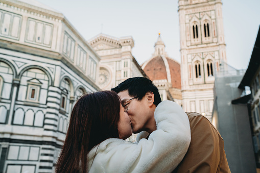 An asian couple in love is kissing in Santa Maria del Fiore square in Florence, Italy. They are enjoying their honeymoon in Italy.