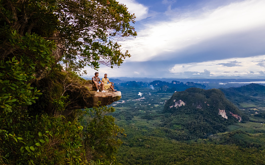 Couple men and women at the edge of a mountain, Dragon Crest mountain Krabi Thailand, Young travelers sits on a rock that overhangs the abyss, Dragon Crest or Khuan Sai at Khao Ngon Nak