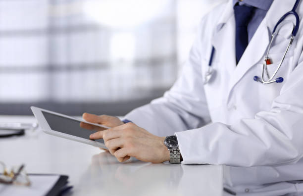 istock Unknown male doctor sitting and working with tablet computer in clinic at his working place, close-up. Young physician at work. Perfect medical service, medicine concept 1464741246