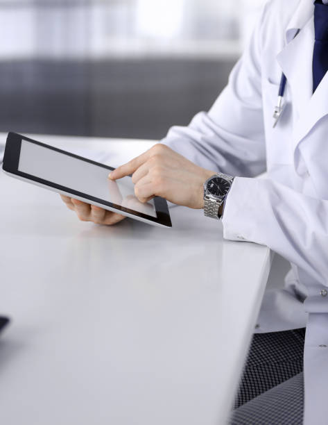 istock Unknown male doctor sitting and working with tablet computer in clinic at his working place, close-up. Young physician at work. Perfect medical service, medicine concept 1464741251
