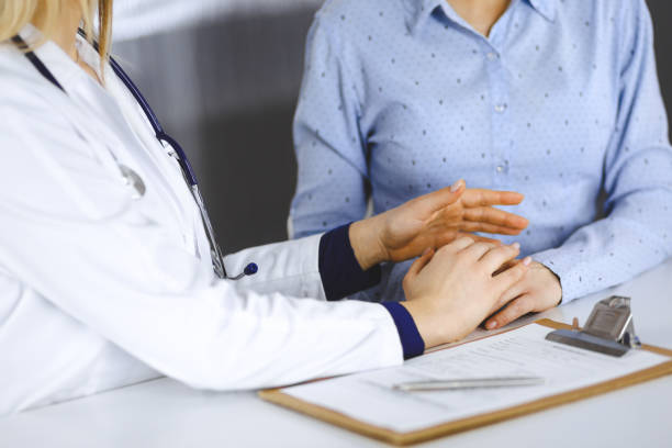 Unknown woman-doctor is holding her patient's hands to reassure a patient, while sitting together at the desk in the cabinet in a clinic. Female physician is using a clipboard and a stethoscope, close-up. Perfect medical service in a hospital. Medicine concept. una doctora desconocida sostiene las manos de su paciente para tranquilizar a un paciente, mientras están sentados juntos en el escritorio en el gabinete de una clínica. la doctora está usando un portapapeles y un estetoscopio, de cerca. servicio médic