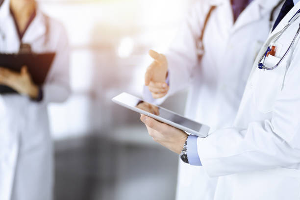 istock Group of unknown doctors use a computer tablet to check up some medical names records, while standing in a sunny hospital office. Physicians ready to examine and help patients. Medical help, insurance in health care 1464741378