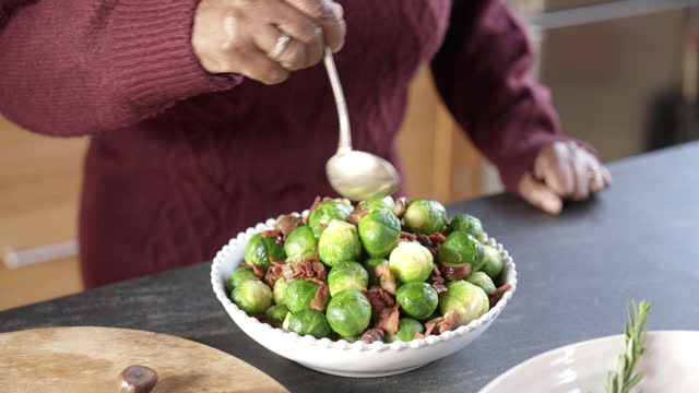 Senior Black woman drizzling olive oil over Brussels sprouts