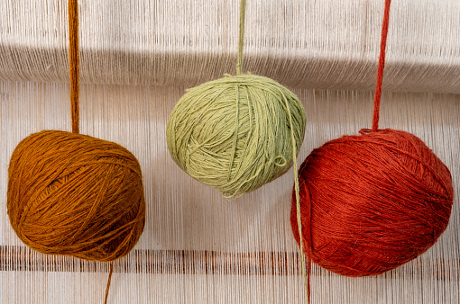 Colorful natural wool yarn balls hanging on the loom with wool yarn background.