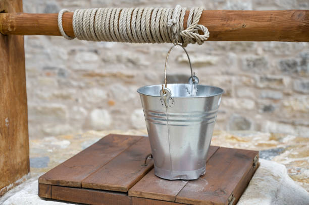 Ancient water well with shiny copper water bucket with stone wall background..