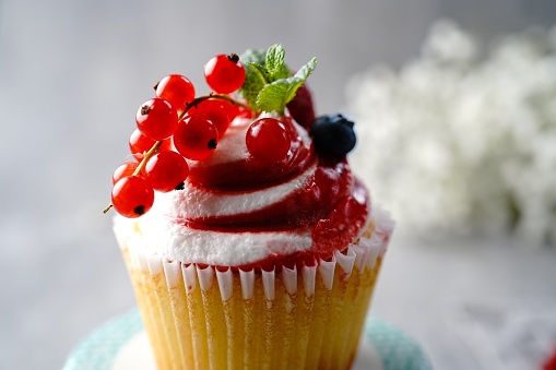 Strawberry shortcake cupcake topped with red currants, blueberries, and raspberries, selective focus